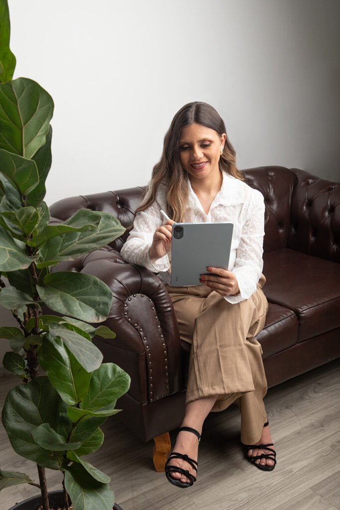 Mulher sorridente usando tablet em sofá de couro marrom.